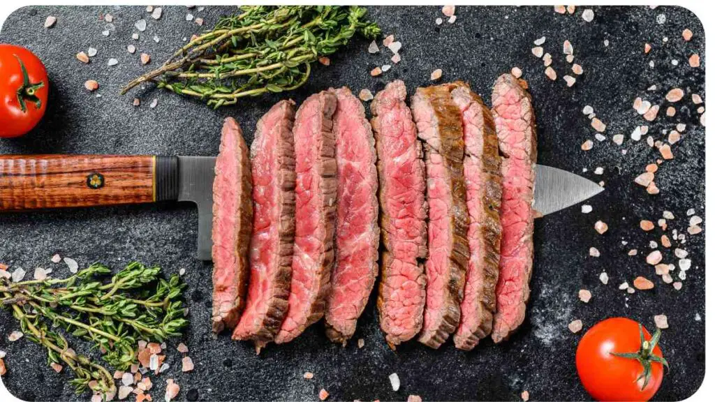 sliced steak on a cutting board with tomatoes and herbs